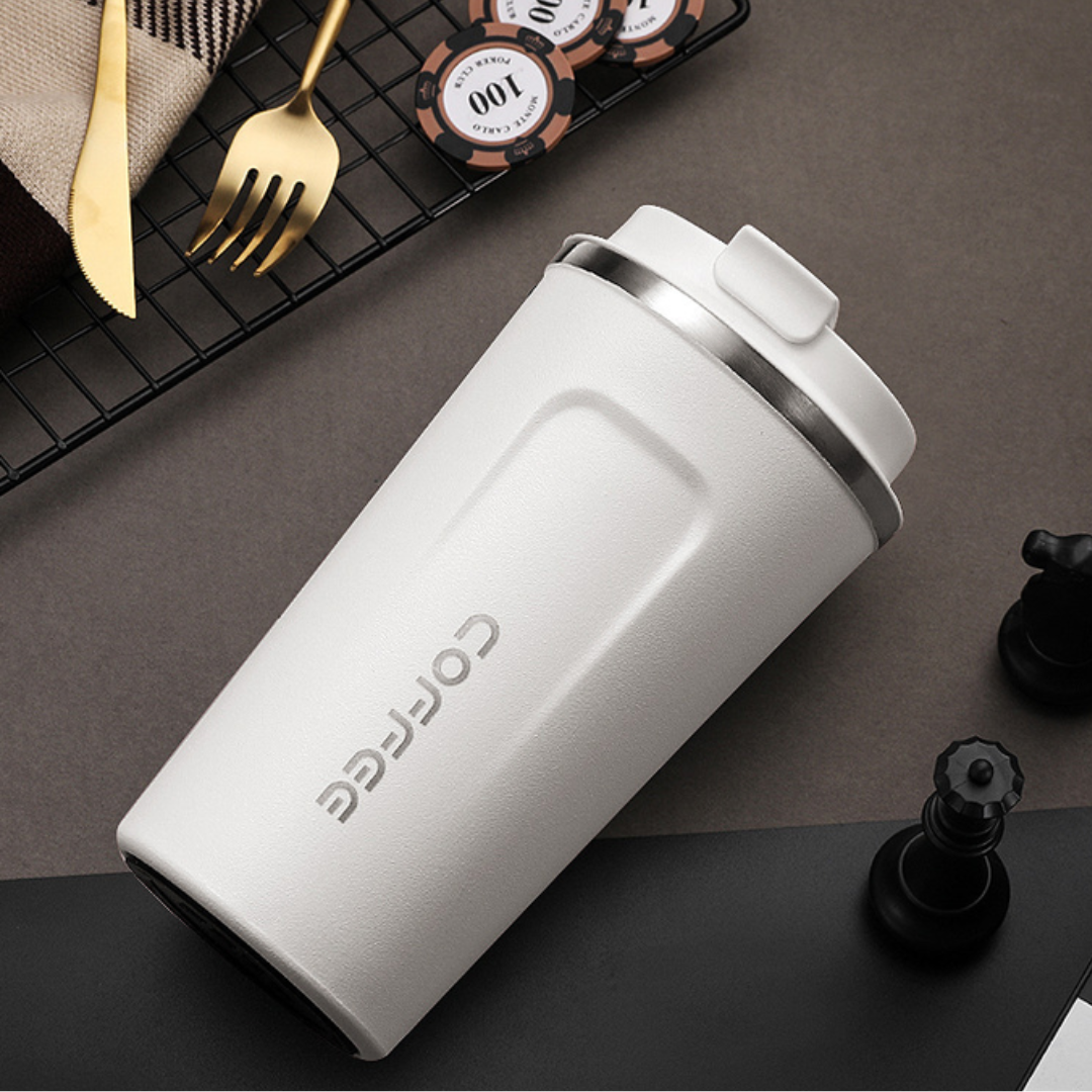 White travel mug with silver lid on a dark surface with gaming items.