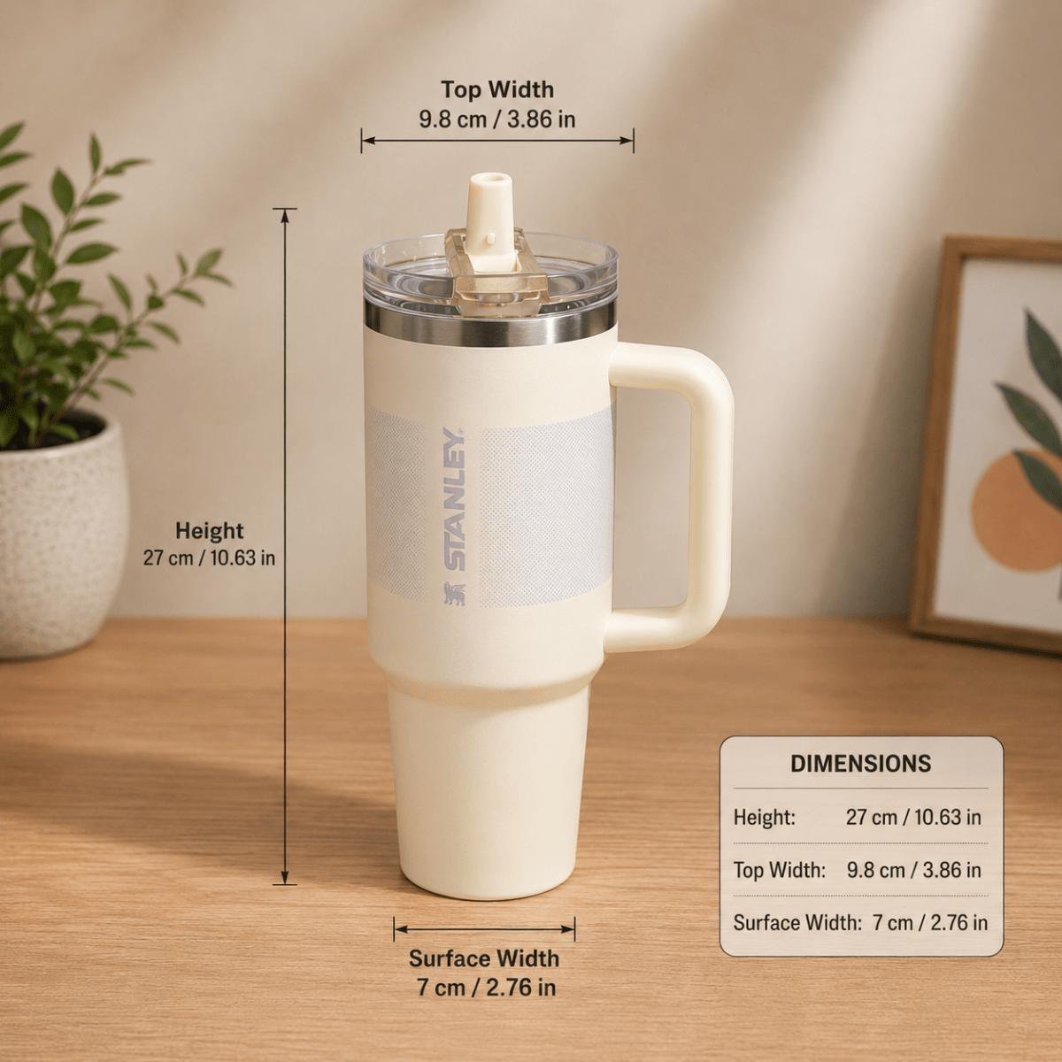 40oz Insulated Stainless Steel TumblerTumblersCrafty CuddleA Stanley insulated tumbler with a handle and lid is shown on a wooden tabletop with overlaid dimension lines and text indicating height, top width, and surface width. A small plant and framed art are blurred in the background.White1.18L tumblertumbler with straw