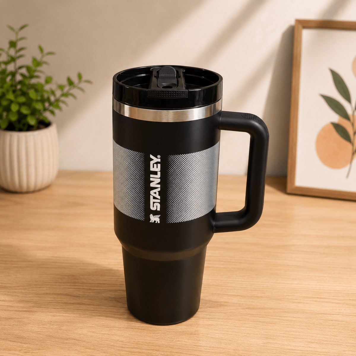 40oz Insulated Stainless Steel TumblerTumblersCrafty CuddleA black Stanley travel mug with a handle and lid, standing on a wooden table in a styled indoor setting with a plant and framed art in the background.Black1.18L tumblertumbler with straw