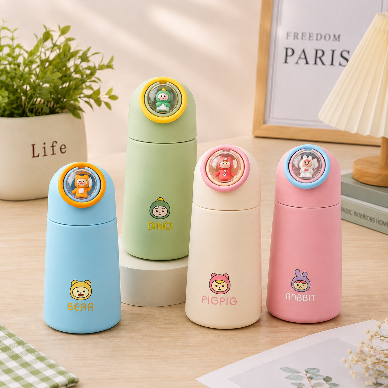 Four cute cartoon water bottles in light blue, mint green, cream, and pink, arranged on small pedestals on a light wood table with decorative props in the background.