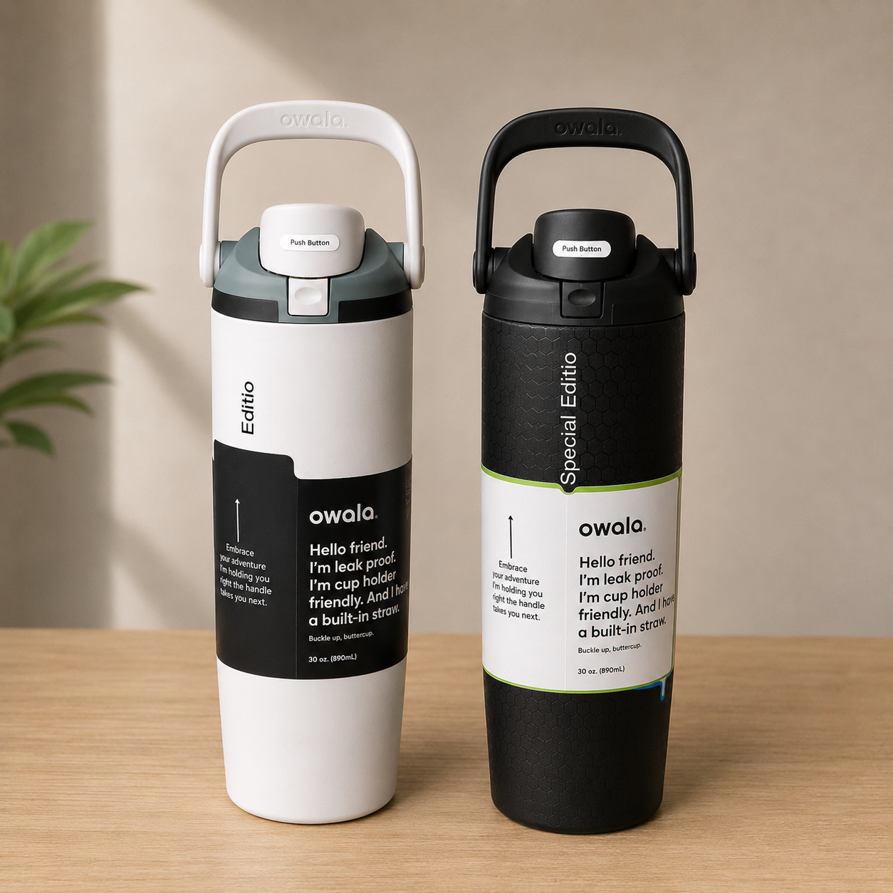 Two Owala insulated travel mugs with carry handles standing side by side on a light wood surface against a beige wall. The left mug is white with a dark gray and black label, and the right mug is black with a white and green label.