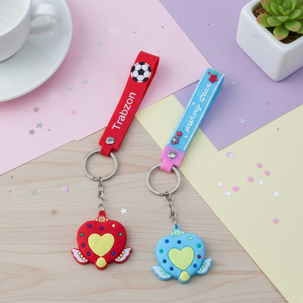 Two colorful keychains on a wooden surface with a cup and plant in the background.