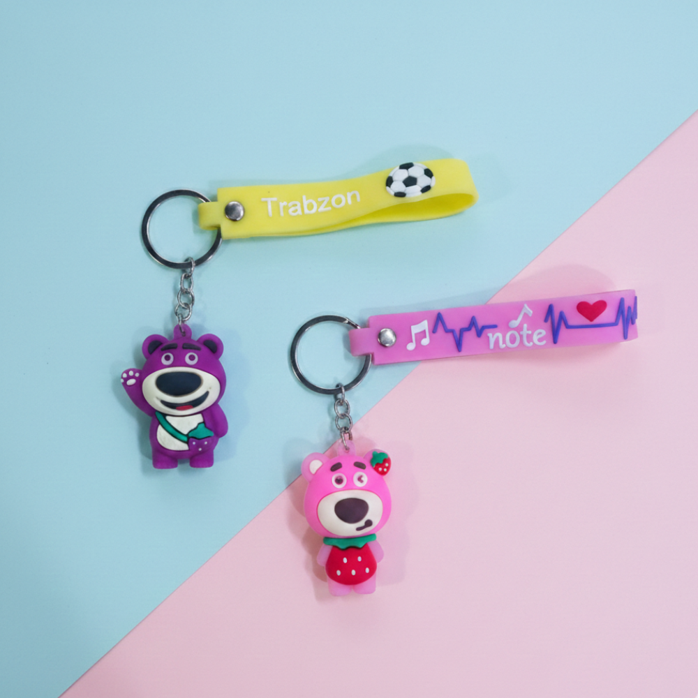 Two keychains with cartoon bear designs on a pink and blue background