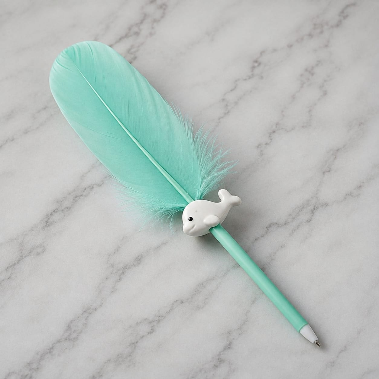 A mint green feather pen with a small white dolphin figurine on the barrel, resting on a white marble surface.