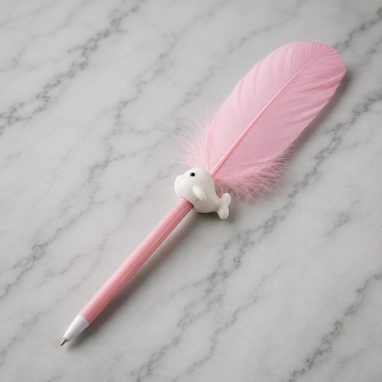 A pink novelty pen with a large pink feather attached to the top and a small white whale-shaped charm, photographed on a light gray marble surface.