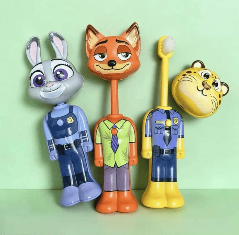 Three cartoon animal-shaped toothbrushes standing upright on a pale green background: a gray rabbit in a blue police outfit on the left, an orange fox in a green shirt in the center, and a yellow tiger in a blue police outfit on the right.