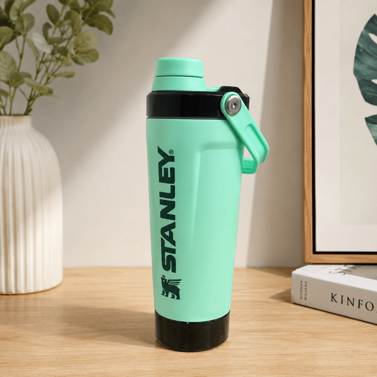 Activate Shaker BottleInsulated Water BottleCrafty CuddleA mint green Stanley water bottle with black accents and a carrying loop, standing on a wooden table with a vase and framed print in the background.Mint GreenShakerBottle ProteinShaker GymBottle FitnessEssentials WaterBottle WorkoutGear LeakproofBottle BPAFree SportsBottle Hydration