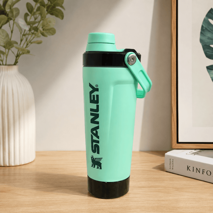 Activate Shaker BottleInsulated Water BottleCrafty CuddleA mint green Stanley water bottle with black accents and a carrying loop, standing on a wooden table with a vase and framed print in the background.Mint GreenShakerBottle ProteinShaker GymBottle FitnessEssentials WaterBottle WorkoutGear LeakproofBottle BPAFree SportsBottle Hydration