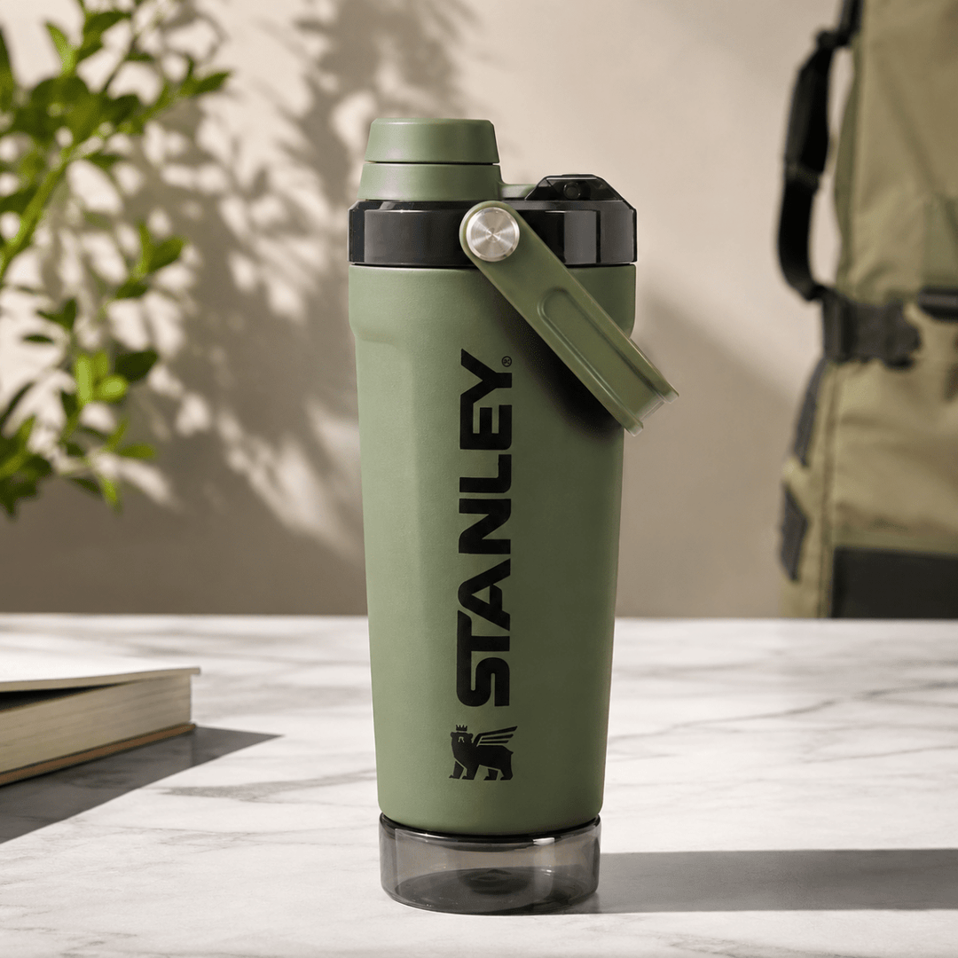 Activate Shaker BottleInsulated Water BottleCrafty CuddleStanley water bottle in olive green with a black logo and a matching green carrying loop, sitting on a light marble surface with a blurred background.Olive GreenShakerBottle ProteinShaker GymBottle FitnessEssentials WaterBottle WorkoutGear LeakproofBottle BPAFree SportsBottle Hydration