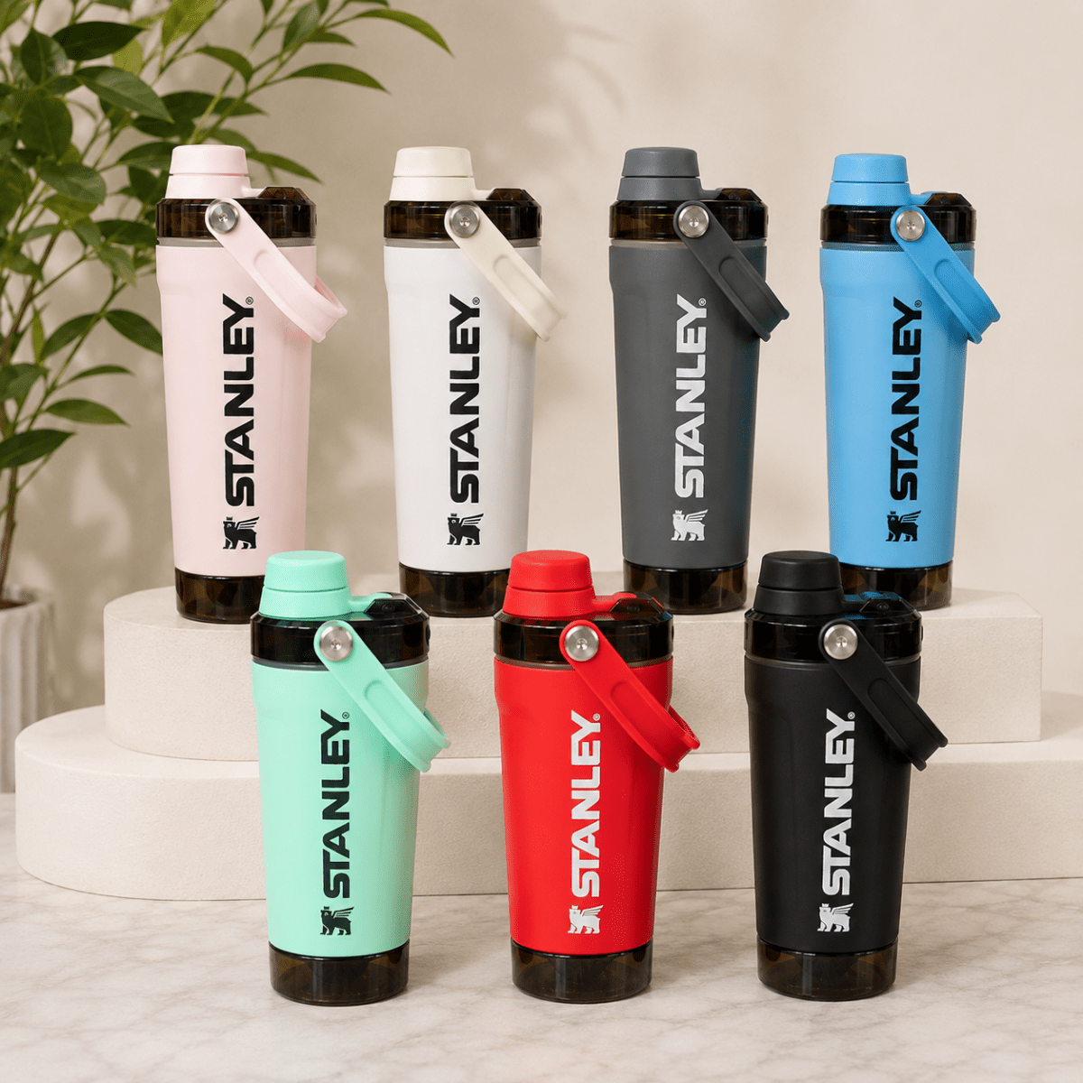 Activate Shaker BottleInsulated Water BottleCrafty CuddleSix Stanley shaker bottles in different colors (pink, white, dark gray, light blue, mint green, red, and black) arranged on white risers and a marble surface with a green plant in the background.Olive GreenShakerBottle ProteinShaker GymBottle FitnessEssentials WaterBottle WorkoutGear LeakproofBottle BPAFree SportsBottle Hydration
