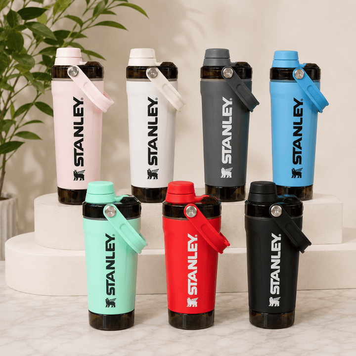 Activate Shaker BottleInsulated Water BottleCrafty CuddleSix Stanley shaker bottles in different colors (pink, white, dark gray, light blue, mint green, red, and black) arranged on white risers and a marble surface with a green plant in the background.Olive GreenShakerBottle ProteinShaker GymBottle FitnessEssentials WaterBottle WorkoutGear LeakproofBottle BPAFree SportsBottle Hydration