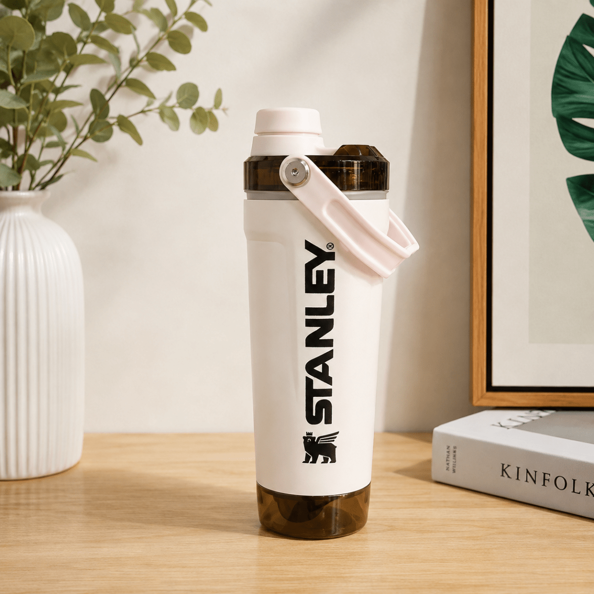 Activate Shaker BottleInsulated Water BottleCrafty CuddleA Stanley water bottle with a white body, black logo, and light pink lid and strap, standing on a wooden table in a styled indoor setting with a vase, framed art, and a book.Cream PinkShakerBottle ProteinShaker GymBottle FitnessEssentials WaterBottle WorkoutGear LeakproofBottle BPAFree SportsBottle Hydration