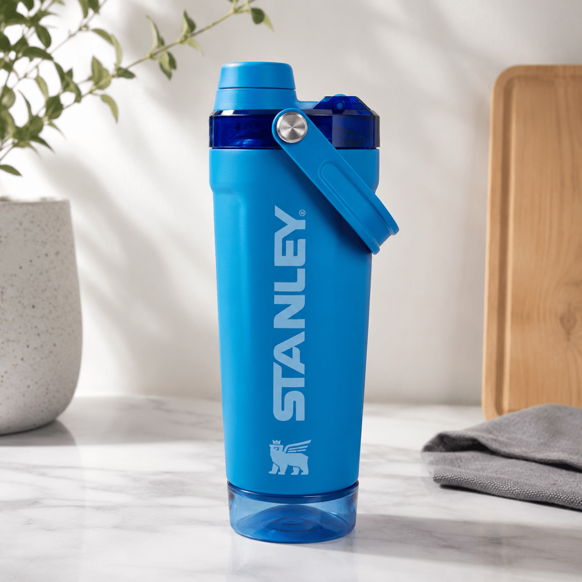 Activate Shaker BottleInsulated Water BottleCrafty CuddleA blue Stanley shaker bottle with a matching blue carrying loop, standing on a white marble countertop with a blurred kitchen background.BlueShakerBottle ProteinShaker GymBottle FitnessEssentials WaterBottle WorkoutGear LeakproofBottle BPAFree SportsBottle Hydration