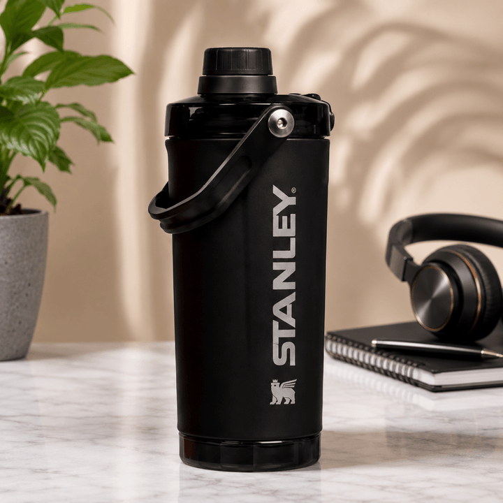 Activate Shaker BottleInsulated Water BottleCrafty CuddleA black Stanley water bottle with a carry loop, standing on a marble tabletop with a plant, headphones, and notebook in the background.BlackShakerBottle ProteinShaker GymBottle FitnessEssentials WaterBottle WorkoutGear LeakproofBottle BPAFree SportsBottle Hydration