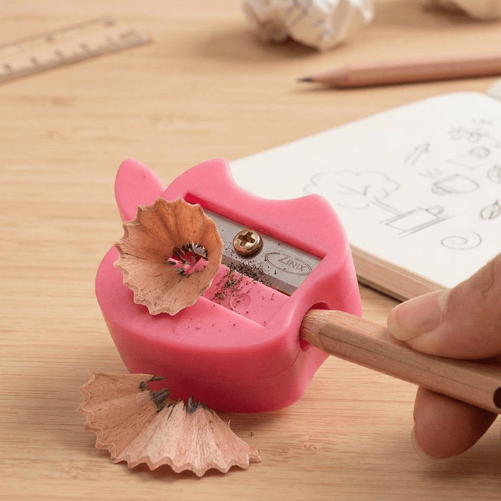 Apple Magic SharpenerCrafty CuddlePink pencil sharpener with a pencil being sharpened on a wooden surface.1
