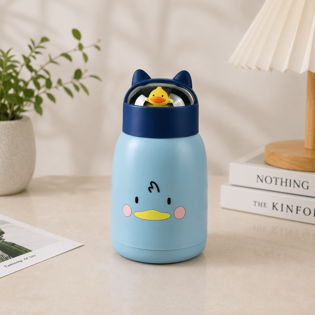Cute Cartoon Glass Water BottleCartoon Kids Water BottleCrafty CuddleA light blue glass bottle with a cartoon duck face and dark blue lid, shown on a tabletop in a styled indoor setting with a plant, lamp, and books.BlueKidsWaterBottle GlassWaterBottle CuteWaterBottle CartoonBottle SchoolEssentials KidsAccessories LeakproofBottle BackToSchool KidsLifestyle CraftyCuddle