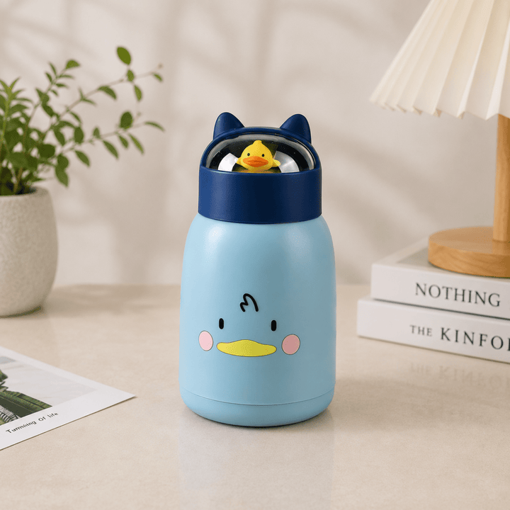 Cute Cartoon Glass Water BottleCartoon Kids Water BottleCrafty CuddleA light blue glass bottle with a cartoon duck face and dark blue lid, shown on a tabletop in a styled indoor setting with a plant, lamp, and books.BlueKidsWaterBottle GlassWaterBottle CuteWaterBottle CartoonBottle SchoolEssentials KidsAccessories LeakproofBottle BackToSchool KidsLifestyle CraftyCuddle