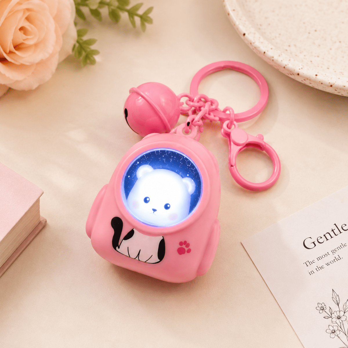 Cute Cartoon LED Keychain with BellKeychainsCrafty CuddleA pink astronaut-shaped keychain toy with a glowing blue window showing a white bear face, attached to a pink bell and key rings, styled on a light beige surface with decorative flowers and a book.CuteKeychain CartoonKeychain BagCharm KeychainCollection KawaiiAccessories CuteAccessories GiftIdeas ReturnGifts StationeryLovers CraftyCuddleStationeryAddict