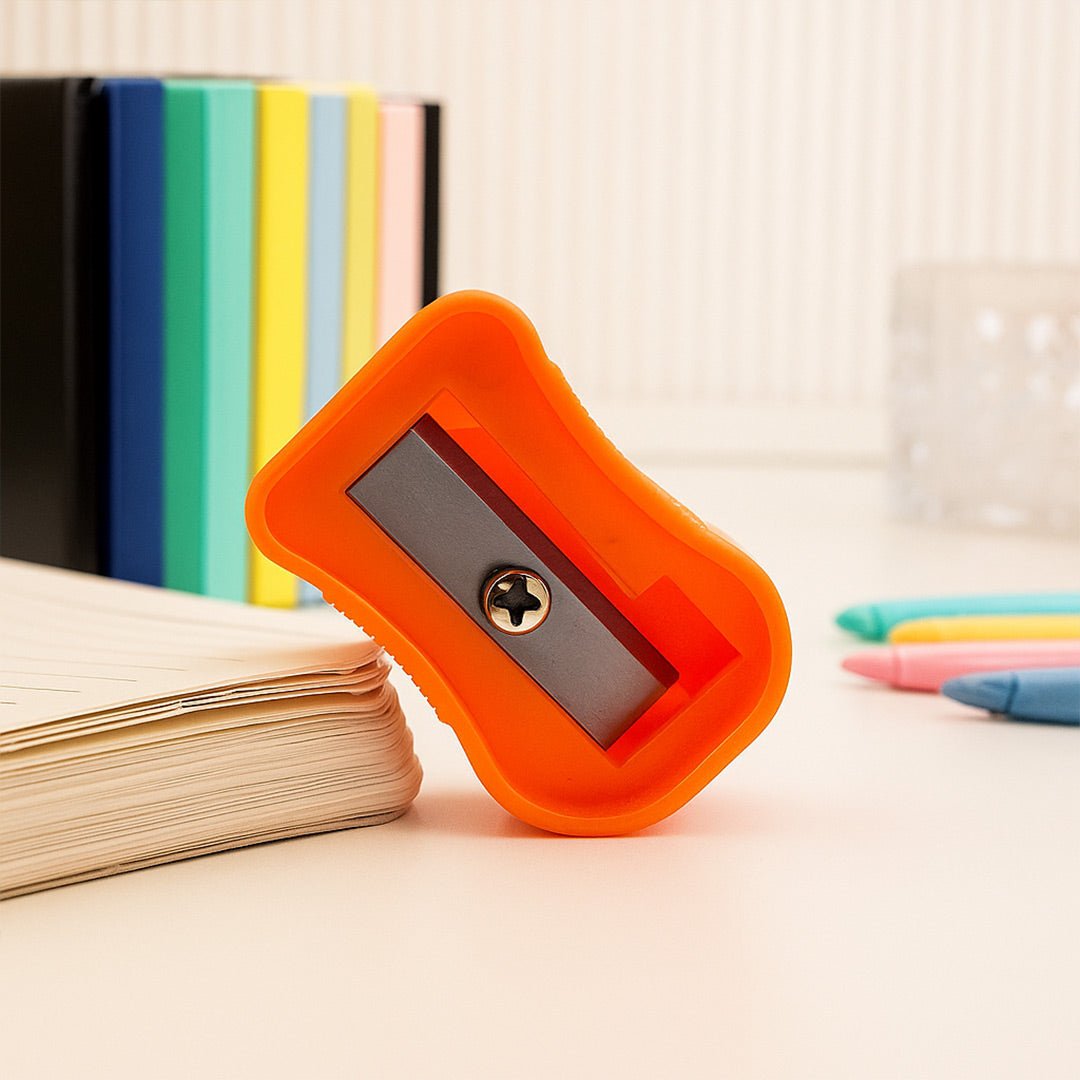Orange pencil sharpener on a desk with books and crayons in the background