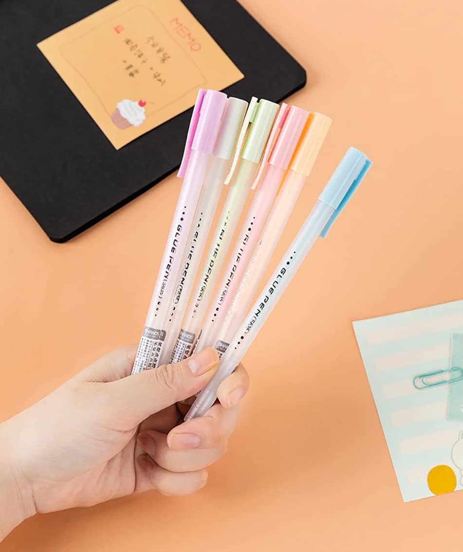 Hand holding colorful pens with a notebook and card in the background on an orange surface
