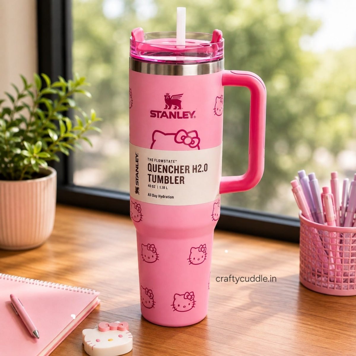 Hello Kitty Stainless Steel TumblerTumblersCrafty CuddleA pink Stanley Quencher H2.0 tumbler with Hello Kitty graphics, featuring a built-in handle and straw, set on a wooden desk next to a notebook, plant, and pens.CreamHello Kitty Tumbler