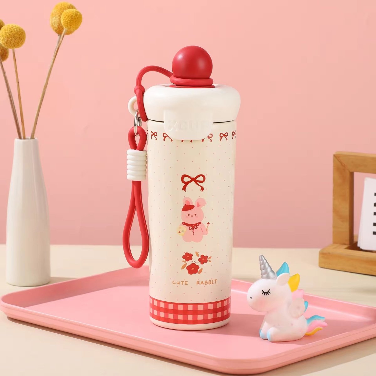 Kids Insulated Water BottleCartoon Kids Water BottleCrafty CuddleA cute white and red insulated water bottle with a rabbit illustration, resting on a pink tray next to a small unicorn figurine. The background is a soft pink wall with a vase of yellow flowers on the left.RedStainlessSteelBottle InsulatedBottle WaterBottle KidsWaterBottle LeakproofBottle ReusableBottle SchoolEssentials TravelBottle HydrationOnTheGo CuteWaterBottle