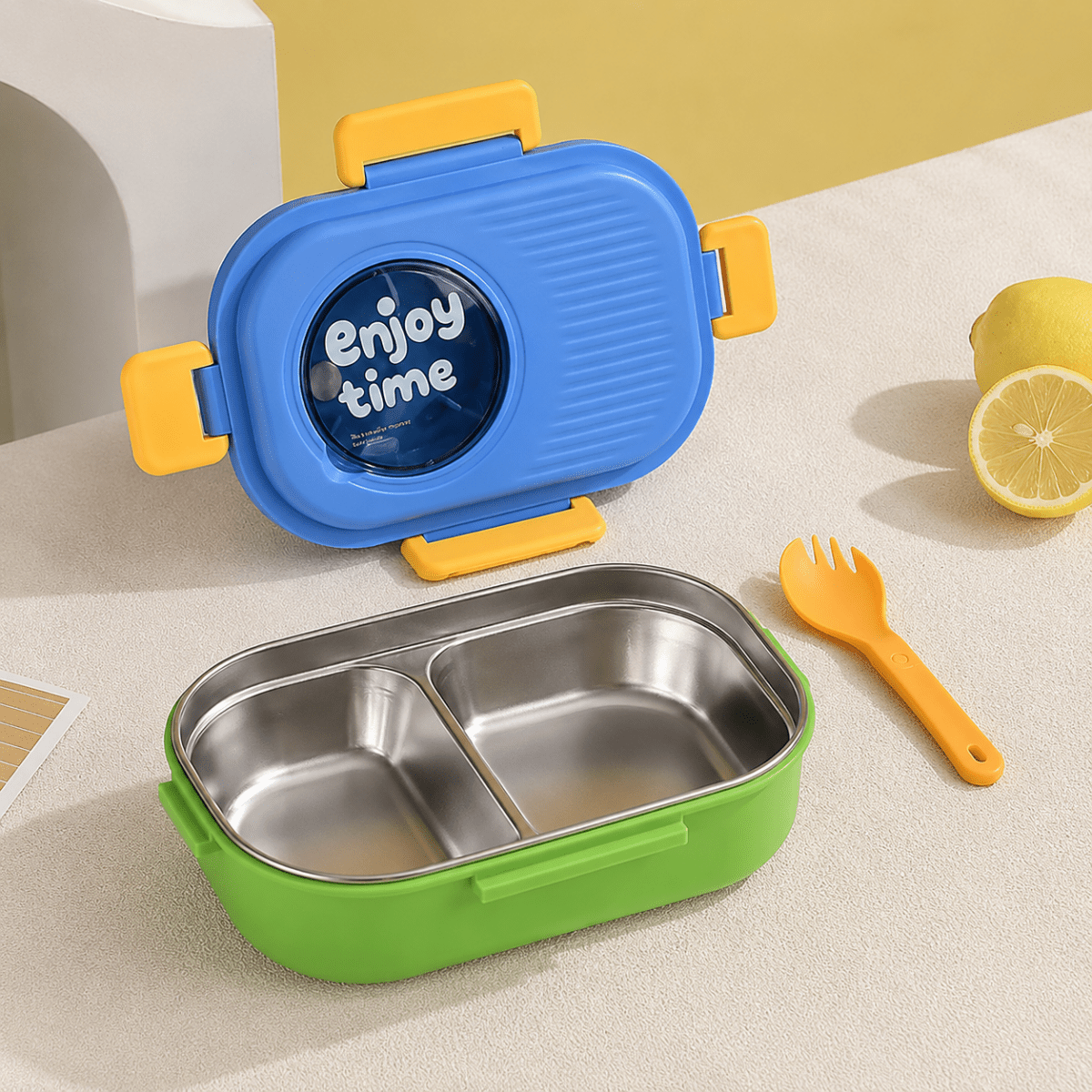 Leakproof Bento Lunch BoxStainless Steel Lunch BoxCrafty CuddleA two-compartment stainless steel lunch box with a bright green base, blue lid, and yellow accents, shown with a matching yellow utensil on a light tabletop. A lemon half and a whole lemon appear in the background, and the lid has a round window reading 'Enjoy time'.BlueLunchBox BentoBox StainlessSteelLunchBox LeakproofLunchBox KidsLunchBox TiffinBox SchoolEssentials OfficeLunch KitchenEssentials LunchGoals