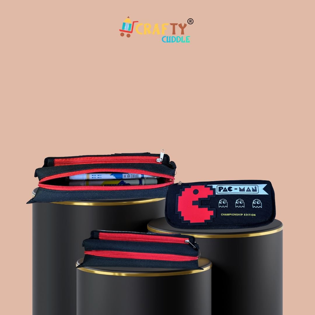 Pac-Man themed black pencil pouch for kids displayed in three angles—front view, top view with red zipper open showing stationery, and side view. Set on black cylindrical stands with a peach background. Crafty Cuddle logo on top.