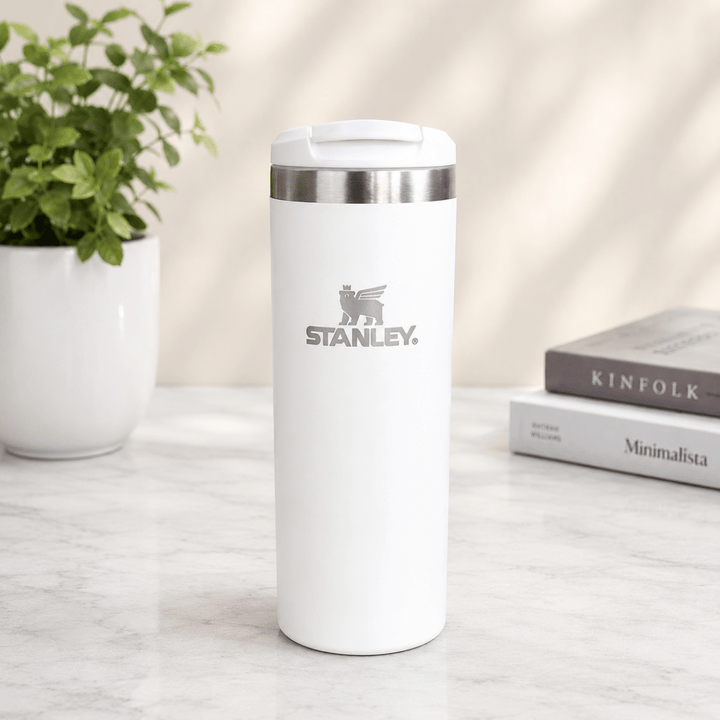 Pastel Stainless Steel Transit MugInsulated Water BottleCrafty CuddleA white Stanley travel tumbler with a stainless steel rim and a gray logo on the front, standing on a light marble surface with a potted plant and books in the background.Cream WhiteTransitMug TravelMug StainlessSteelMug CoffeeMug TravelTumbler InsulatedMug HotAndCold ReusableMug OfficeEssentials DailyUseMug