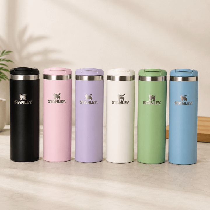 Pastel Stainless Steel Transit MugInsulated Water BottleCrafty CuddleSix Stanley travel tumbler thermoses in different colors (black, pink, lavender, off-white, sage green, and sky blue) lined up on a light wooden surface against a warm beige background.Pastel PinkTransitMug TravelMug StainlessSteelMug CoffeeMug TravelTumbler InsulatedMug HotAndCold ReusableMug OfficeEssentials DailyUseMug