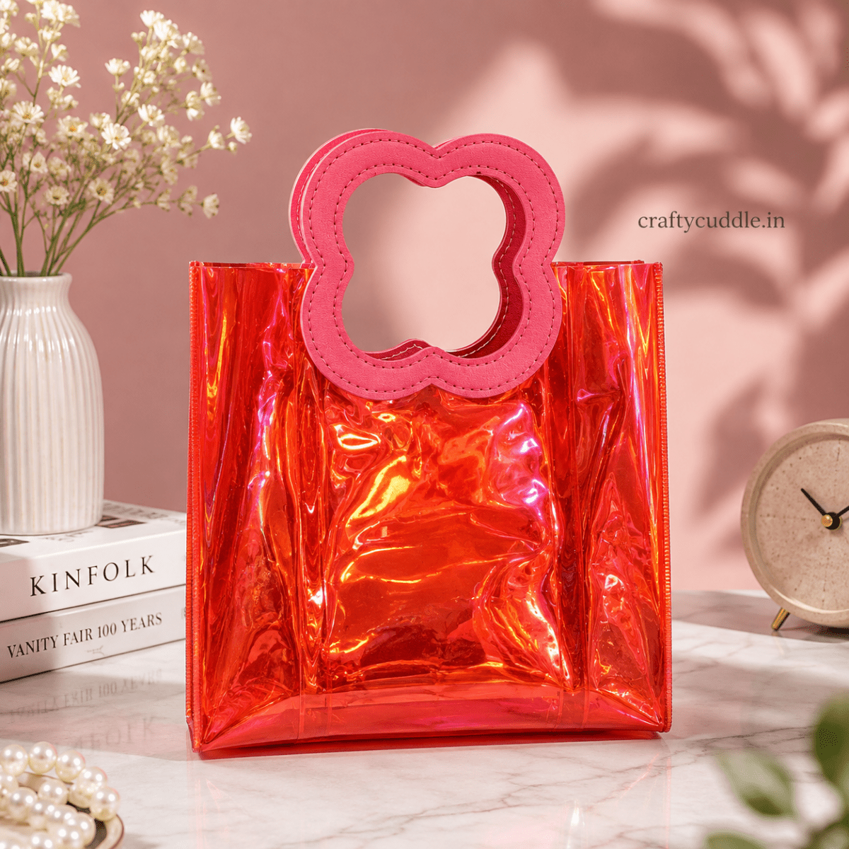 Pretty Shimmer Tote BagTransparent bagCrafty CuddleA shiny translucent red-orange tote bag with a red flower-shaped handle, styled on a marble surface with a pink background and decorative props.RedGiftHampers GiftPackaging GiftBag IridescentBag GiftIdeas ReturnGifts PartyFavours BirthdayGifts FestiveGifting GiftWrap TrendyBags ReusableBag