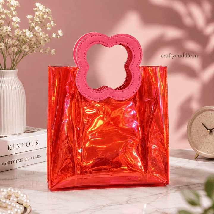 Pretty Shimmer Tote BagTransparent bagCrafty CuddleA shiny translucent red-orange tote bag with a red flower-shaped handle, styled on a marble surface with a pink background and decorative props.RedGiftHampers GiftPackaging GiftBag IridescentBag GiftIdeas ReturnGifts PartyFavours BirthdayGifts FestiveGifting GiftWrap TrendyBags ReusableBag