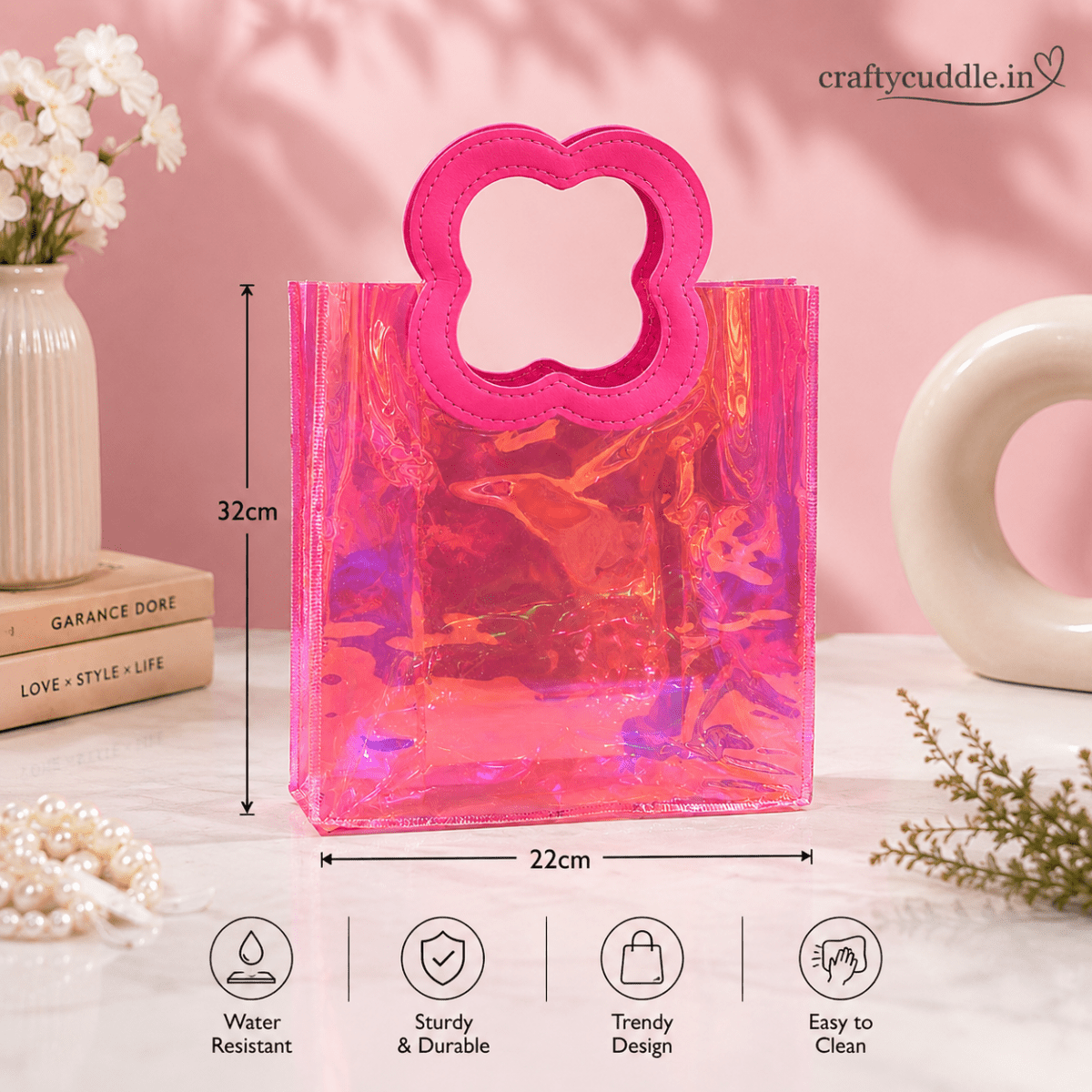 Pretty Shimmer Tote BagTransparent bagCrafty CuddleA translucent pink holographic tote bag with a flower-shaped handle, shown on a styled pink background with dimension markers (32cm height, 22cm width) and feature icons below for water resistance, durability, trendy design, and easy cleaning. The brand name craftycuddle.WhiteGiftHampers GiftPackaging GiftBag IridescentBag GiftIdeas ReturnGifts PartyFavours BirthdayGifts FestiveGifting GiftWrap TrendyBags ReusableBag