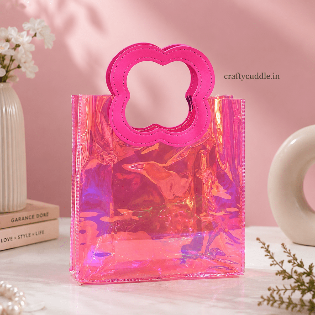 Pretty Shimmer Tote BagTransparent bagCrafty CuddleA translucent holographic pink tote bag with a bright pink flower-shaped handle, styled on a white marble surface with a pink background and decorative props.PinkGiftHampers GiftPackaging GiftBag IridescentBag GiftIdeas ReturnGifts PartyFavours BirthdayGifts FestiveGifting GiftWrap TrendyBags ReusableBag