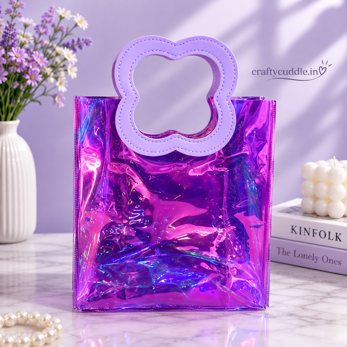Pretty Shimmer Tote BagTransparent bagCrafty CuddleA shiny holographic purple tote bag with a lavender flower-shaped handle, styled on a marble surface with decorative props including a vase of flowers, books, and a candle.PurpleGiftHampers GiftPackaging GiftBag IridescentBag GiftIdeas ReturnGifts PartyFavours BirthdayGifts FestiveGifting GiftWrap TrendyBags ReusableBag
