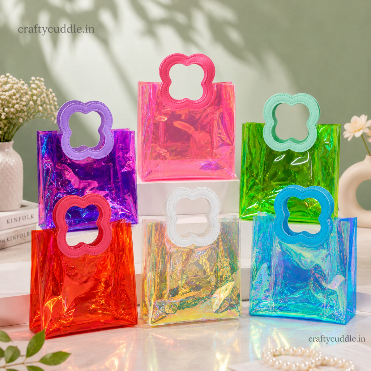 Pretty Shimmer Tote BagTransparent bagCrafty CuddleSix small holographic plastic gift bags with flower-shaped handles in assorted bright colors, arranged on white display blocks against a soft light green background with decorative flowers and shadows.PinkGiftHampers GiftPackaging GiftBag IridescentBag GiftIdeas ReturnGifts PartyFavours BirthdayGifts FestiveGifting GiftWrap TrendyBags ReusableBag