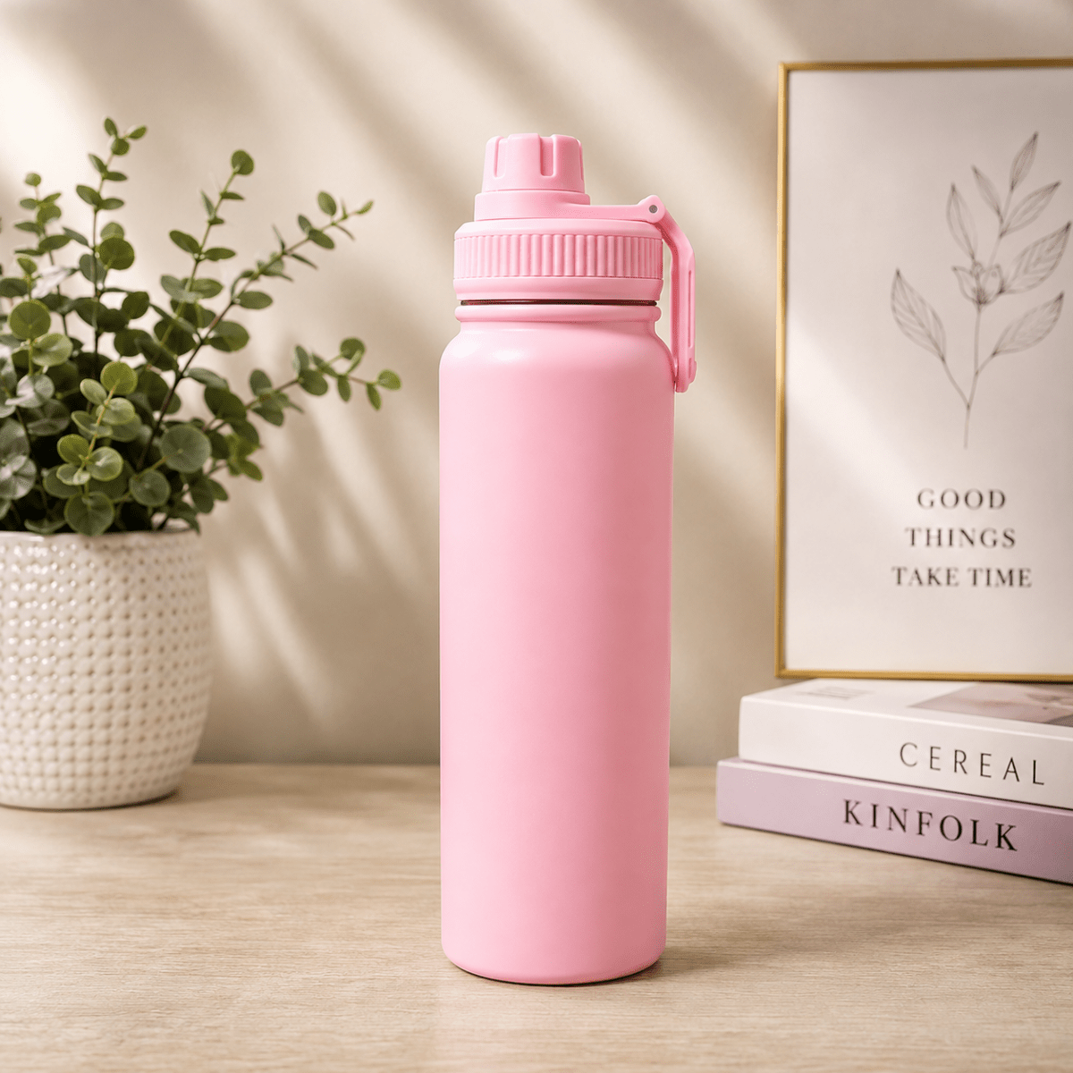 Stainless Steel Vacuum Water Bottle with Carry HandleInsulated Water BottleCrafty CuddleA matte pink reusable water bottle with a matching pink screw-top lid and carry loop, standing on a light wood tabletop. A potted green plant and a framed print reading 'GOOD THINGS TAKE TIME' sit behind it, with two stacked books visible on the right.PinkVacuumBottle WaterBottle InsulatedBottle StainlessSteelBottle HotAndColdBottle TravelBottle GymBottle LeakProofBottle HydrationEssentials ReusableBottle