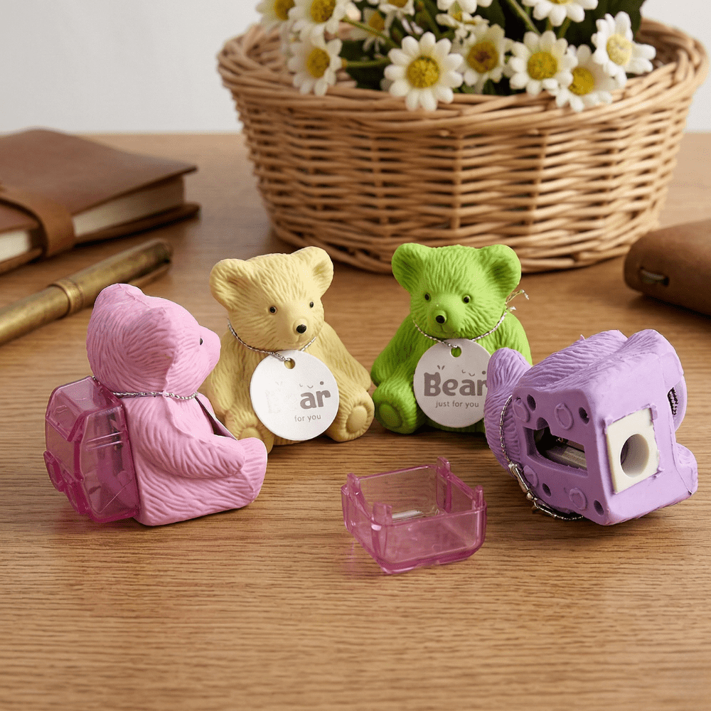 Teddy Bear Eraser &amp; SharpenerCrafty CuddleFour bear - shaped sharpeners in pink, yellow, green, and purple on a wooden surface with a basket of flowers in the background.Teddy Eraser Sharpener-11