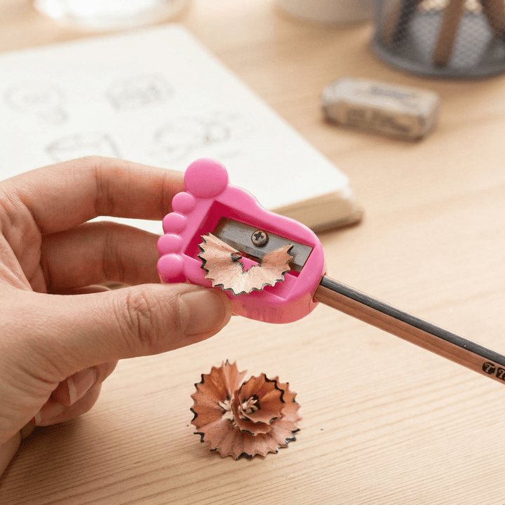 Tiny Toes SharpenerCrafty CuddlePink pencil sharpener with a pencil being sharpened on a wooden surface.1