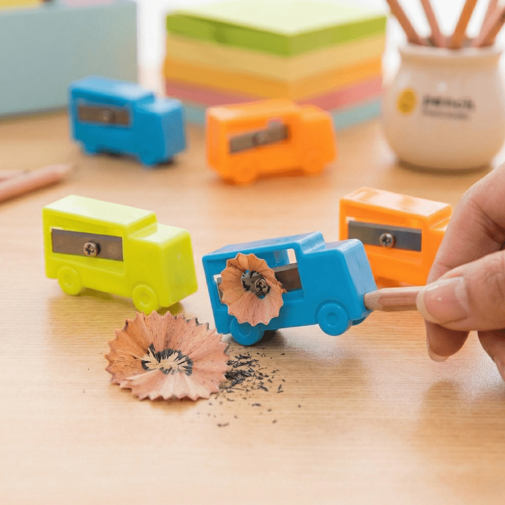 Tiny Truck SharpenerCrafty CuddleColorful pencil sharpeners on a wooden surface with a hand using one of them.1