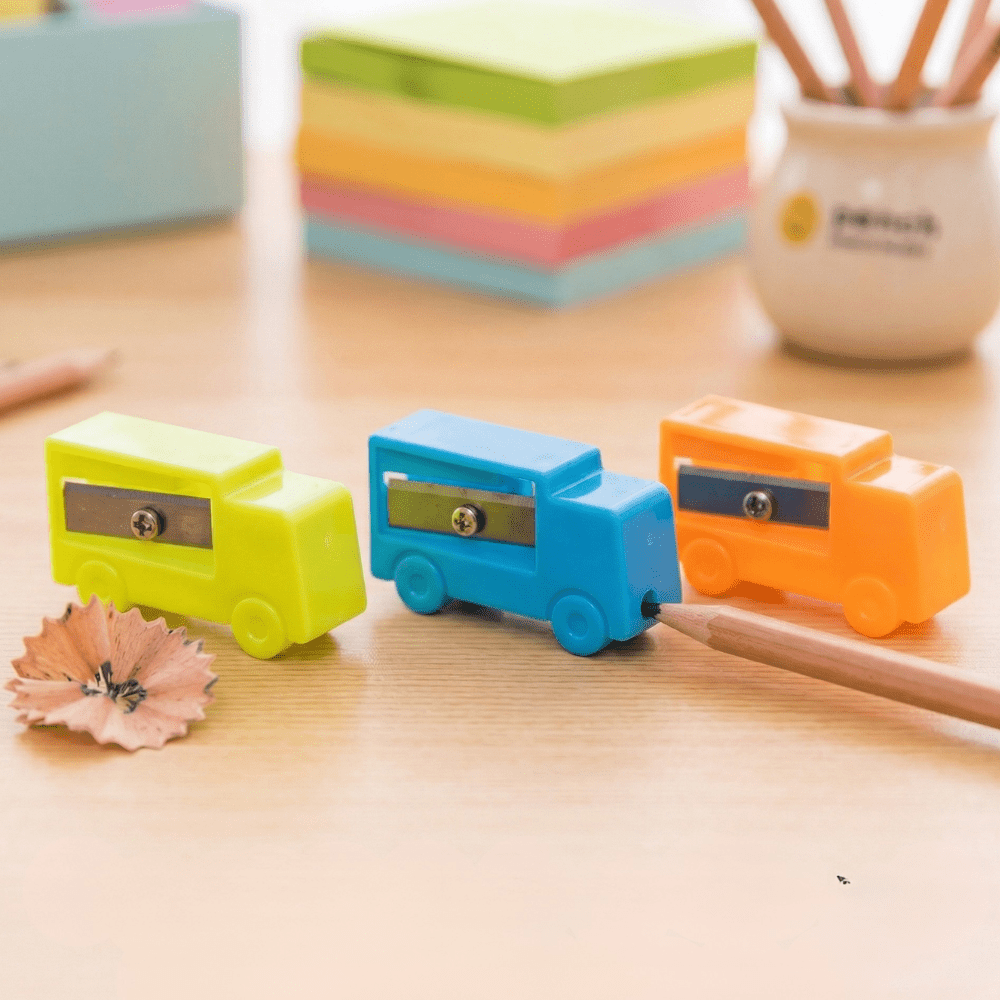 Tiny Truck SharpenerCrafty CuddleThree colorful pencil sharpeners shaped like cars on a wooden surface with pencils and paper in the background.1