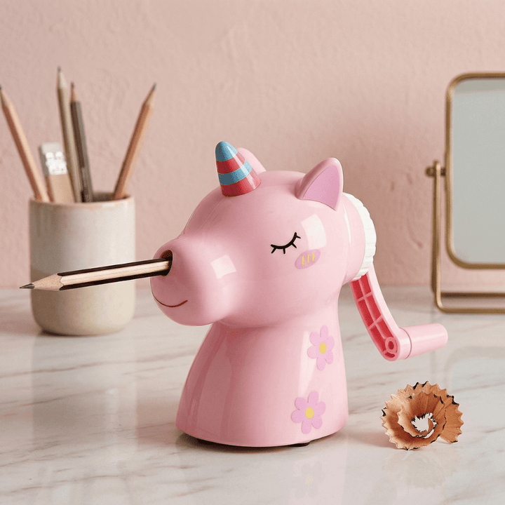 Unicorn Manual Pencil SharpenerCrafty CuddlePink unicorn - shaped pencil sharpener with a pencil inserted, on a light wooden surface with a pink background.Unicorn Sharpener PinkPink