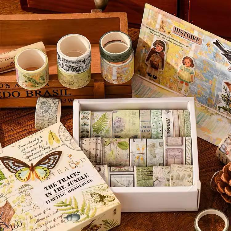 Washi Tape Box of 20 – Jungle Traces SeriesCRAFTY CUDDLECollection of washi tape rolls on a wooden surface with a book and magazine.